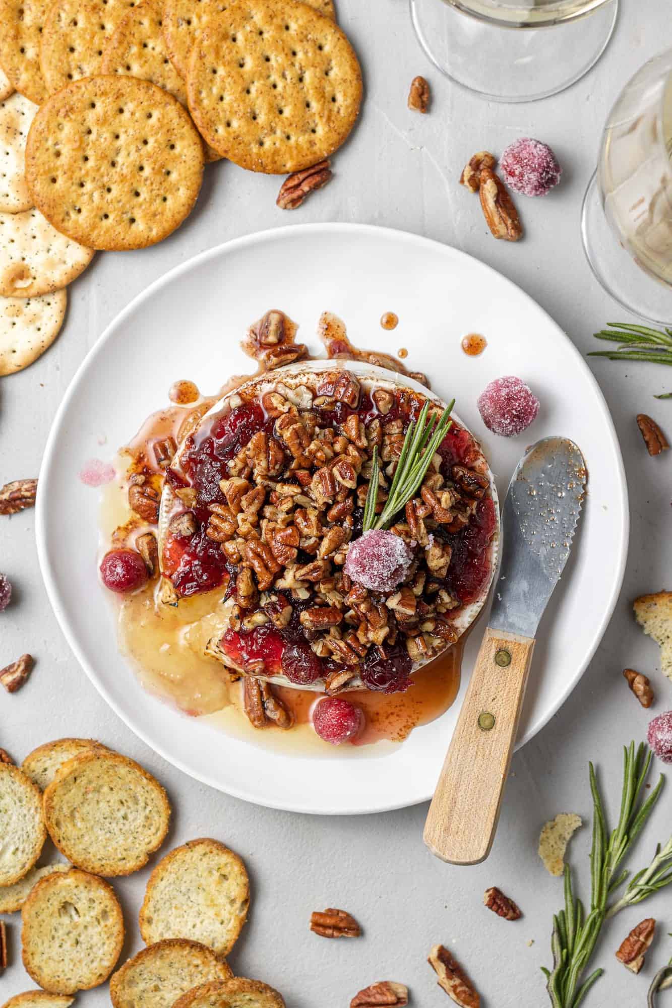 Overhead view of brie topped with cranberries and pecans, garnished with fresh rosemary.