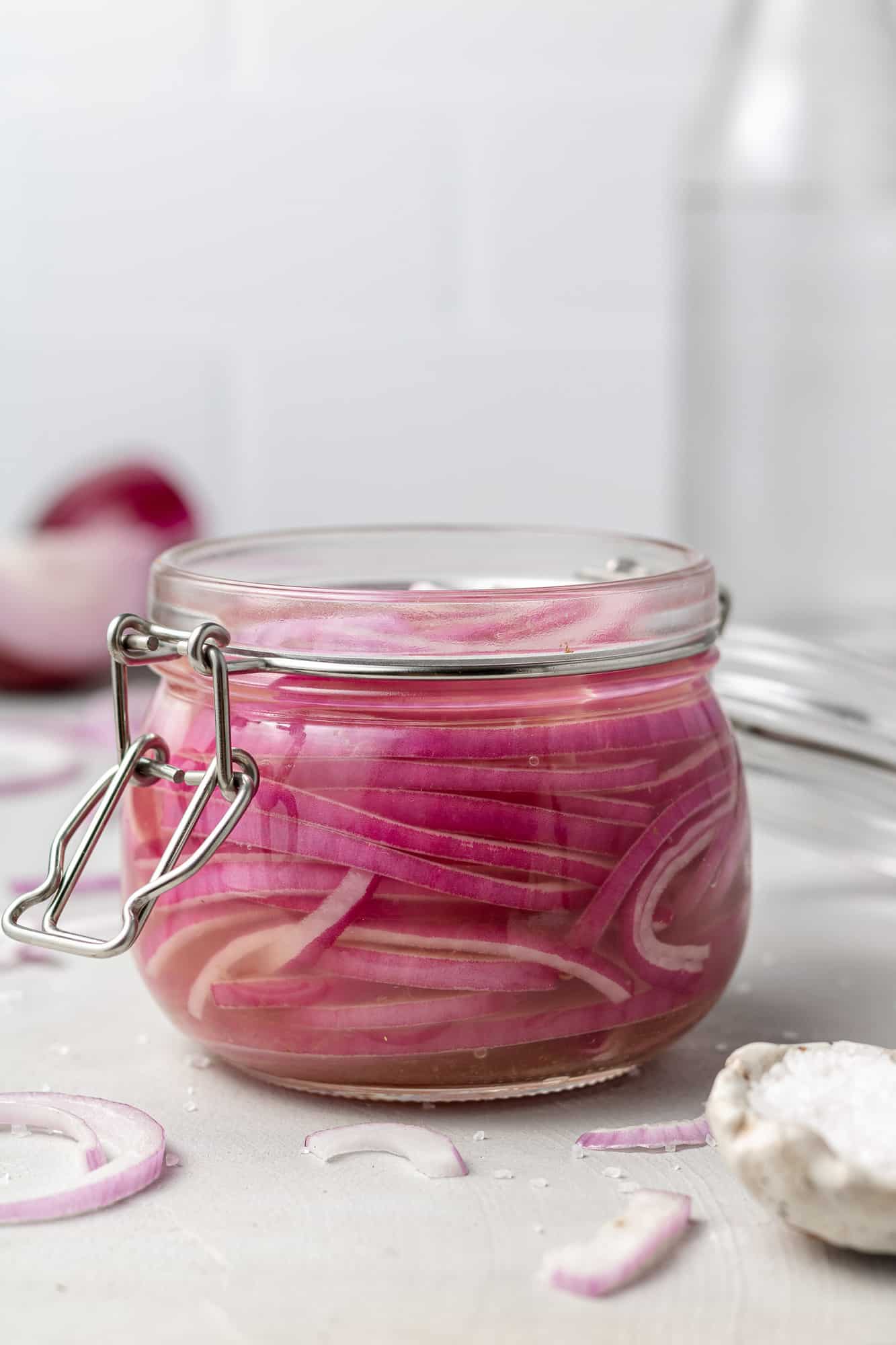 Sliced red onions in pickling solution in small glass jar.