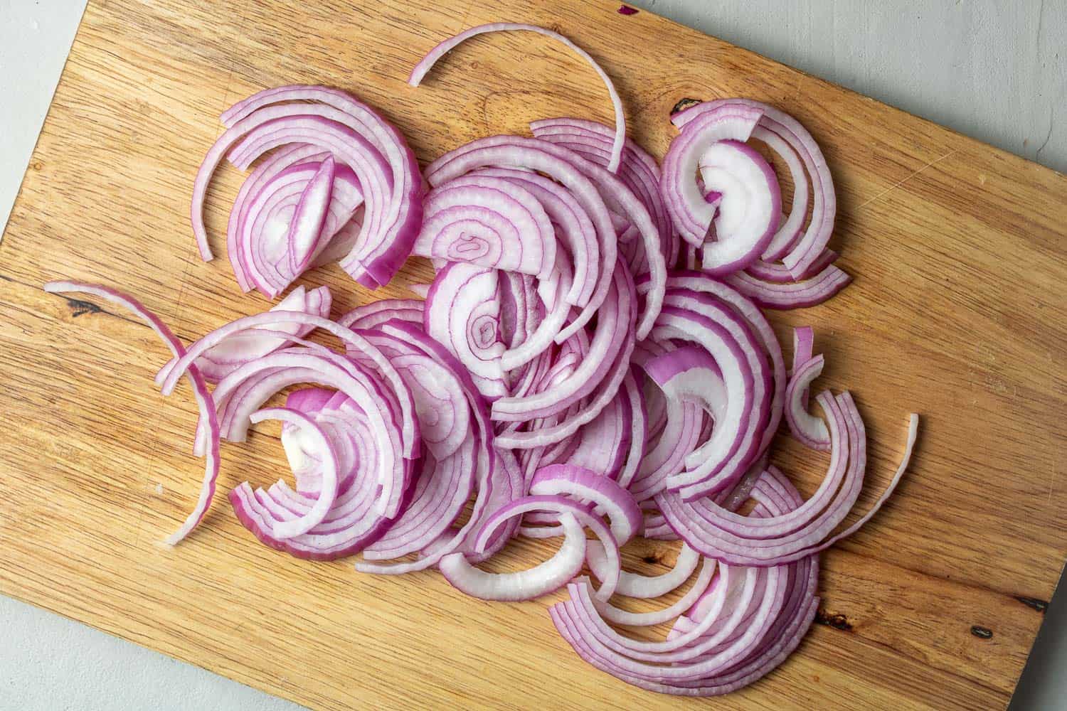 Sliced red onions on a wood or bamboo cutting board.