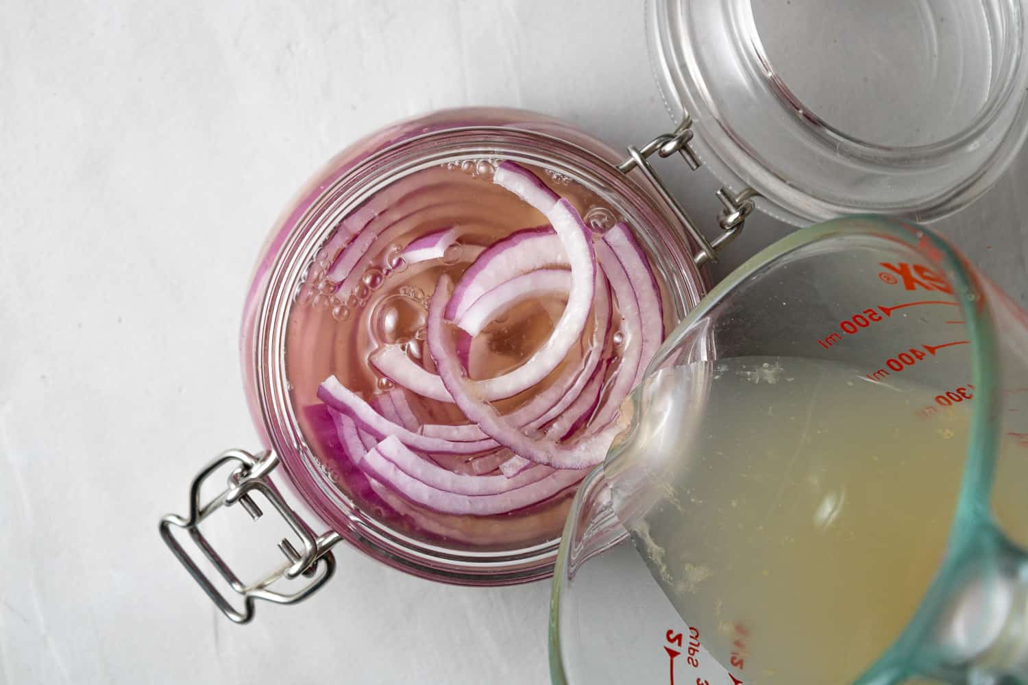 Pickling liquid being poured over sliced onions in a jar.