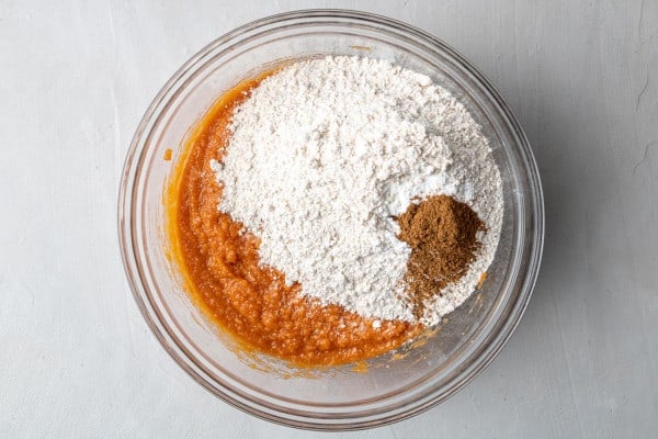 Dry ingredients added to the wet ingredients in a glass mixing bowl.