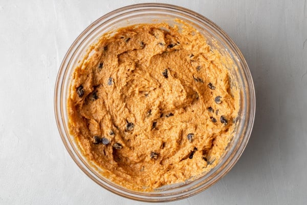 Pumpkin muffin batter in a clear glass mixing bowl.