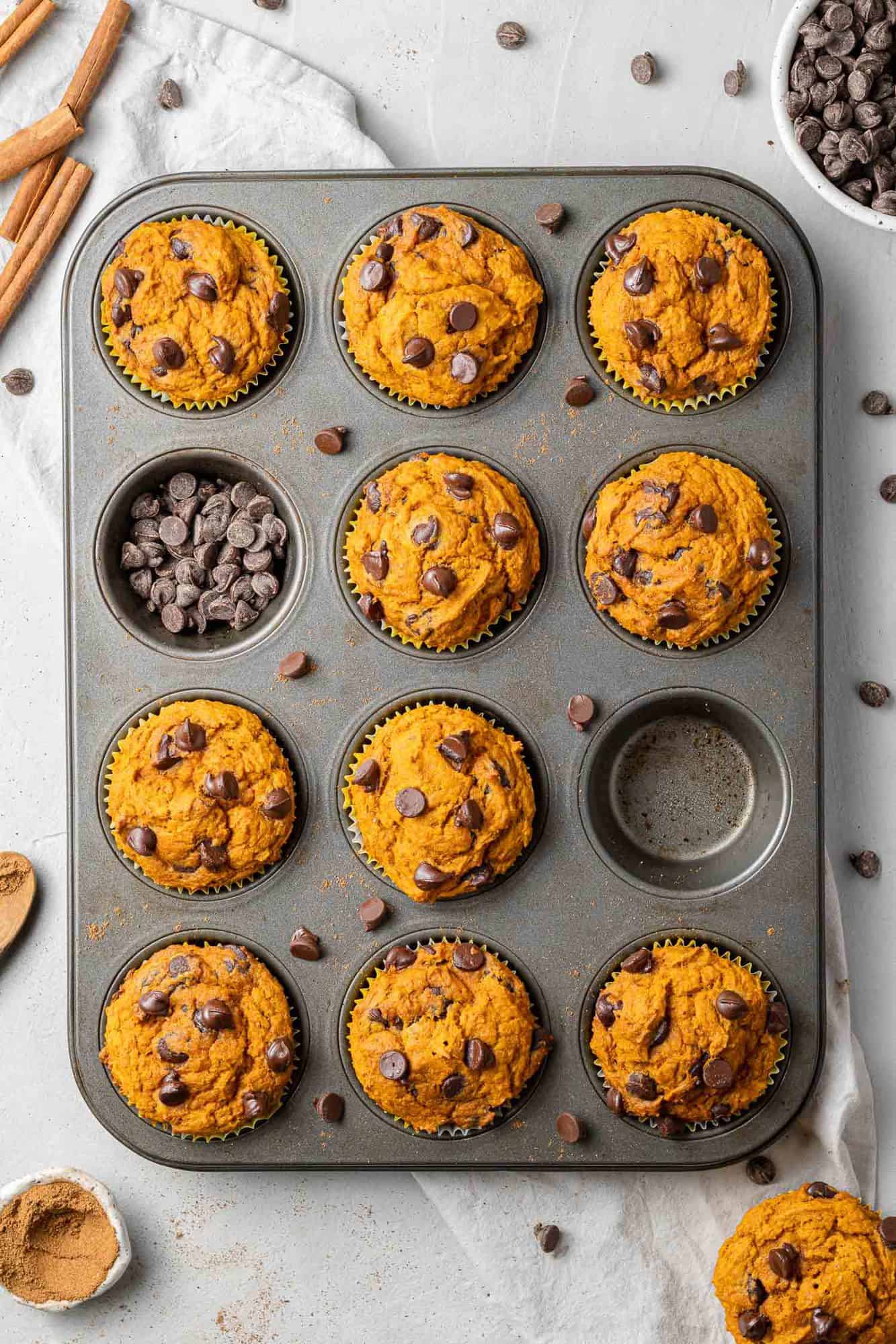 Overhead view of pumpkin chocolate chip muffins in a muffin pan, with two muffins missing.
