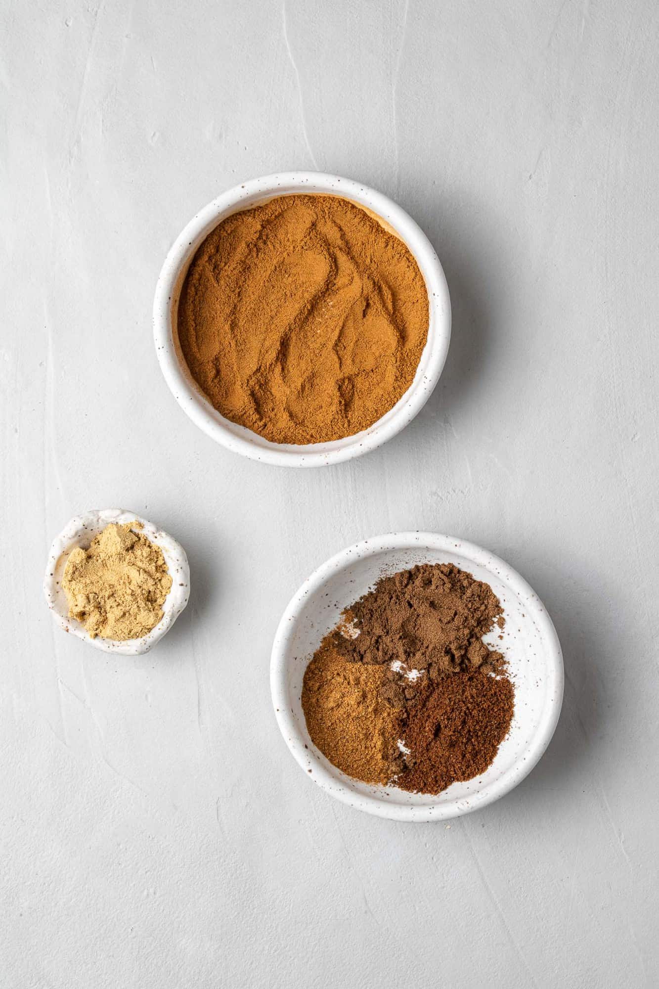 Spices in separate bowls on a light grey background.