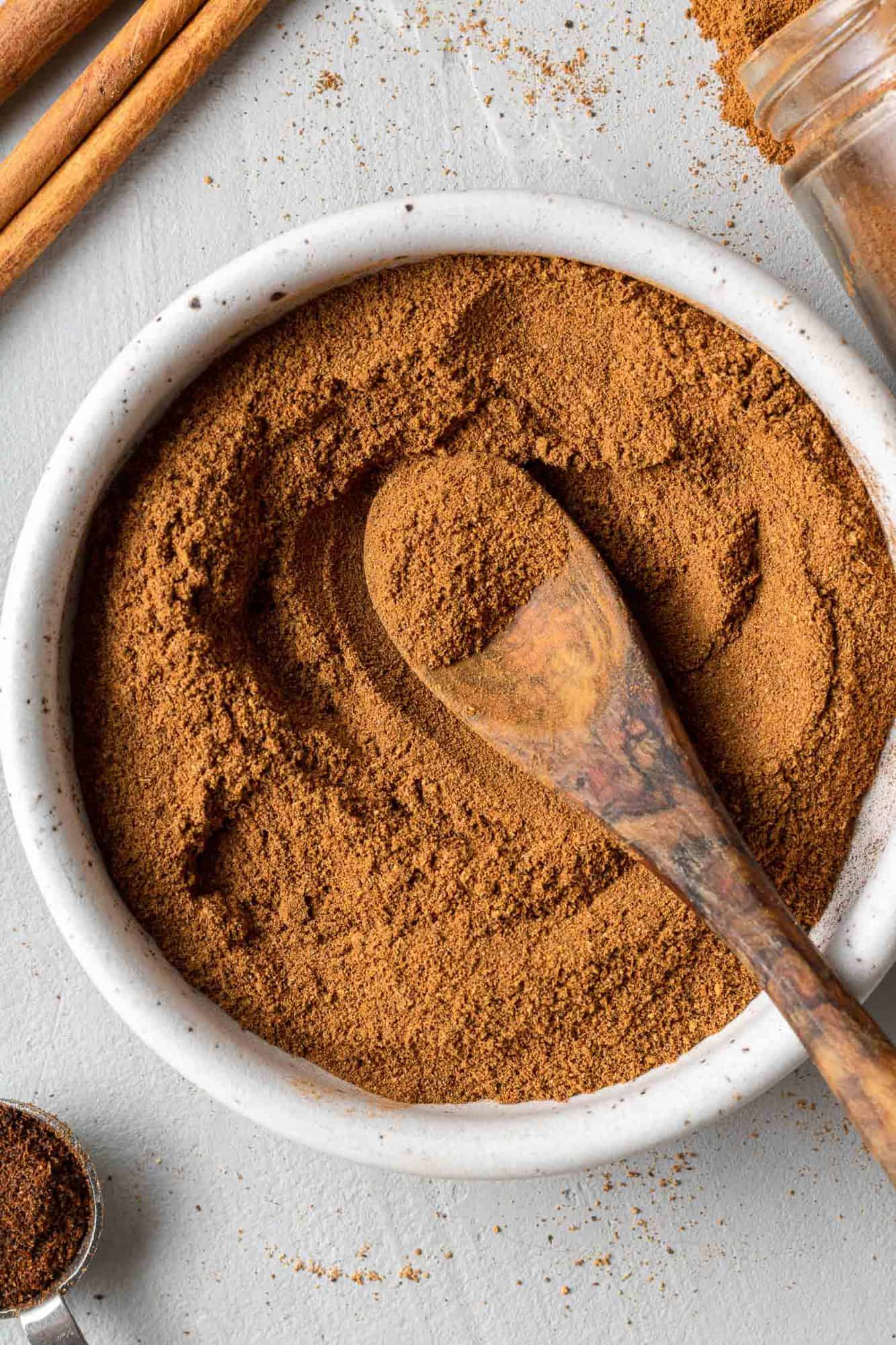 Wooden spoon in a small white bowl of pumpkin pie spice.