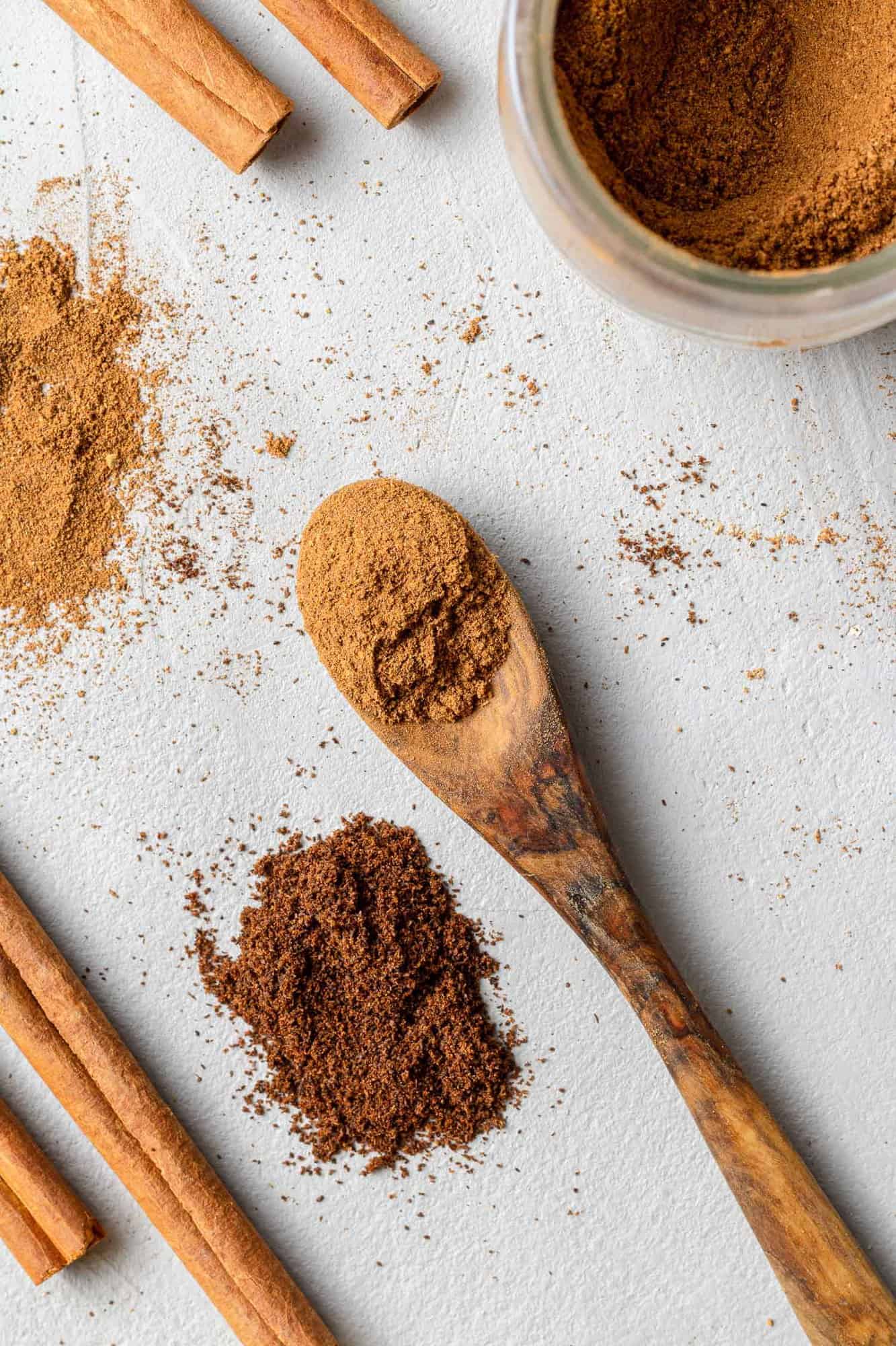 Brown spices on a tiny wooden spoon, other spices nearby.