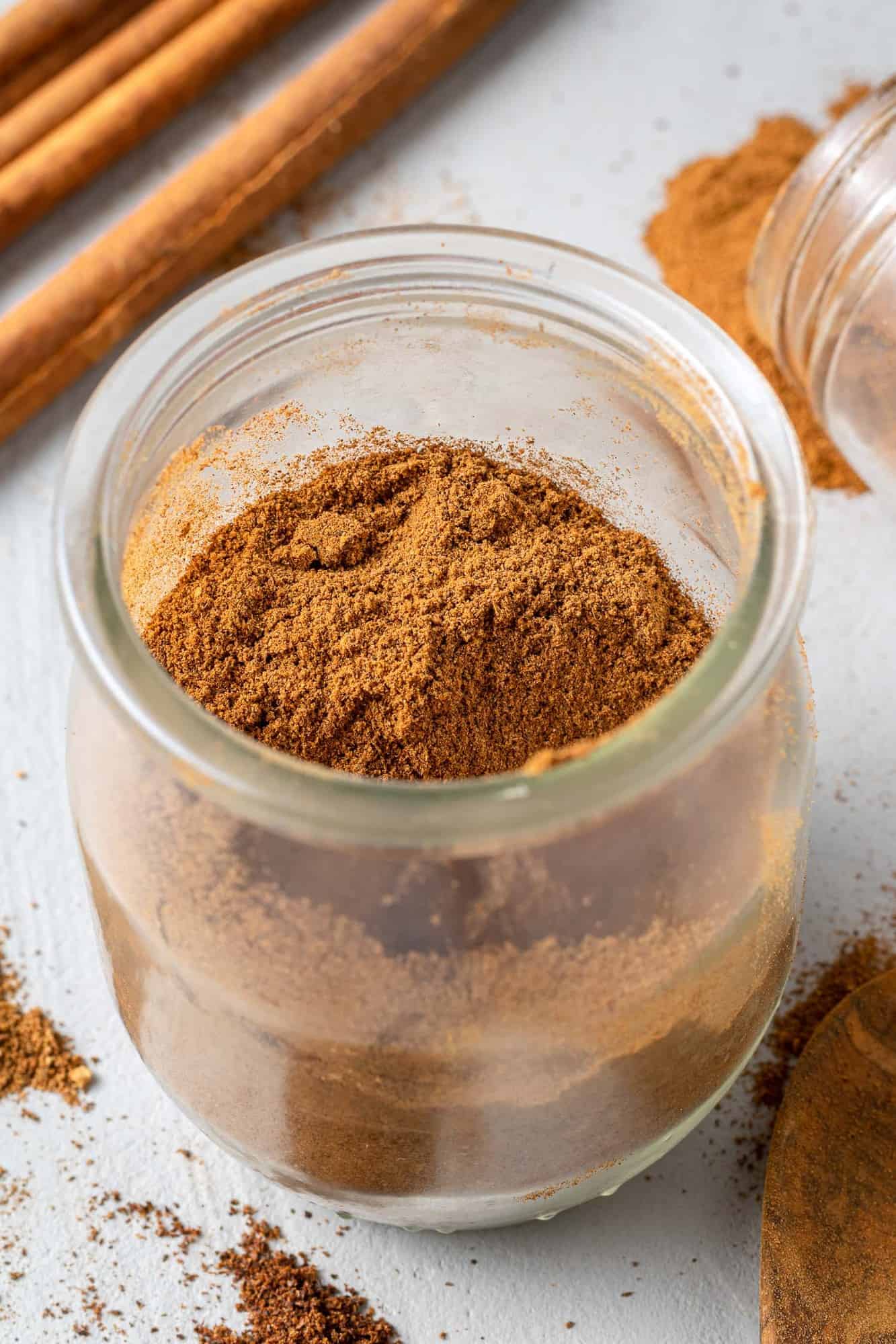 Pumpkin pie spice in a small jar, cinnamon sticks nearby.