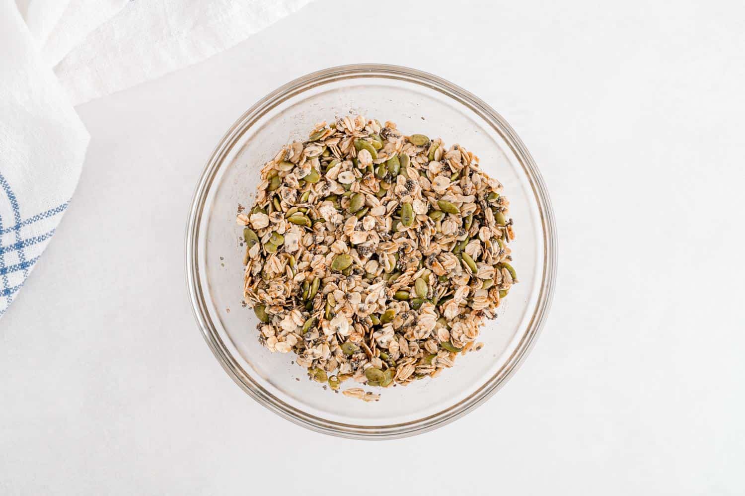 Topping ingredients including oat and pumpkin seeds in a small clear glass bowl.