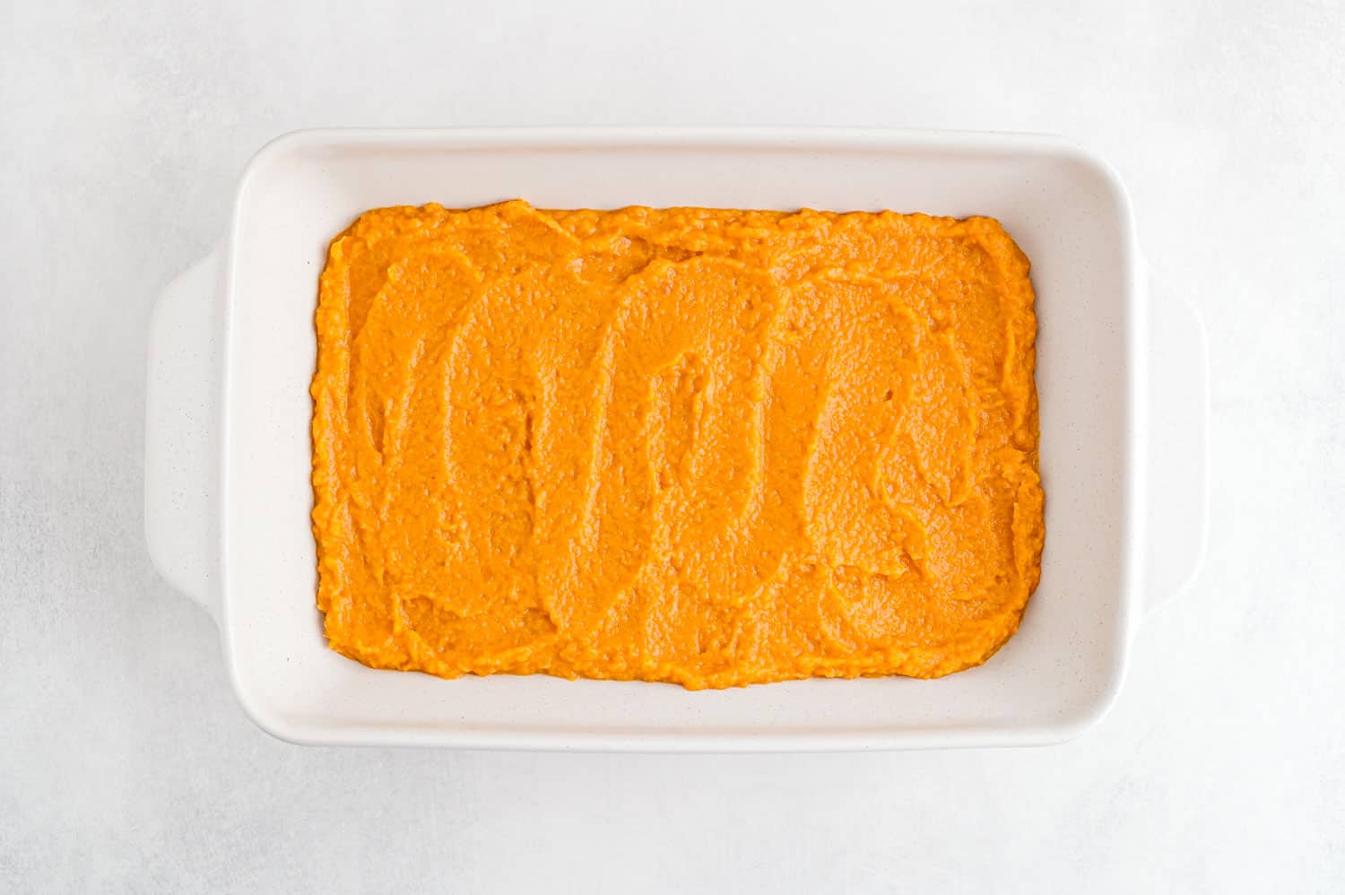 Mashed sweet potatoes spread into a white casserole dish.