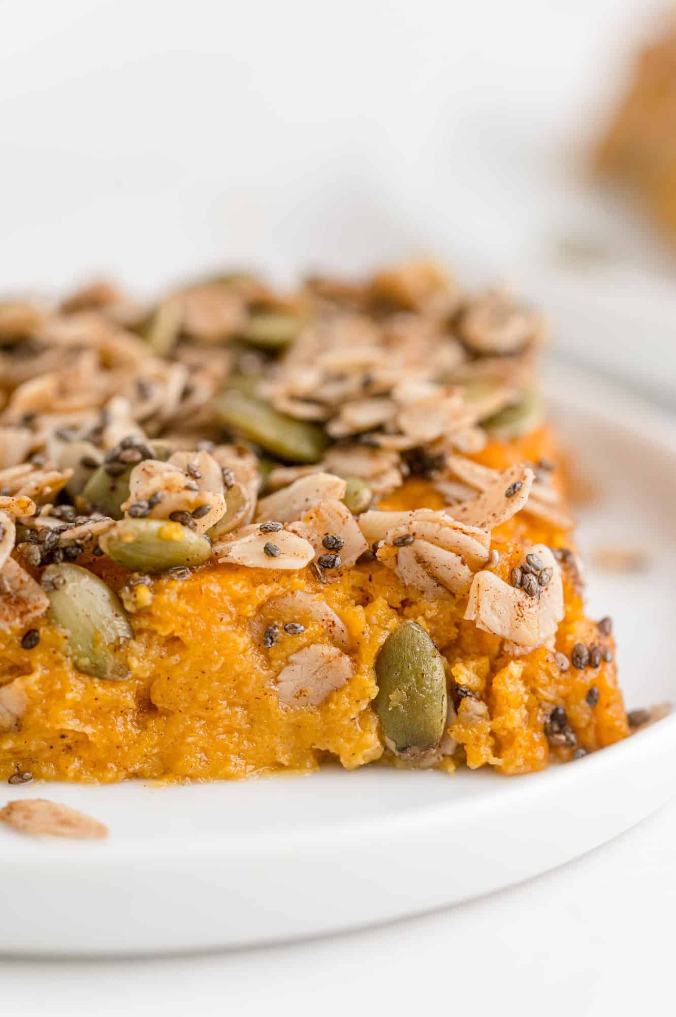 Slice of healthy sweet potato casserole topped with chia seeds, oats, and pepitas.