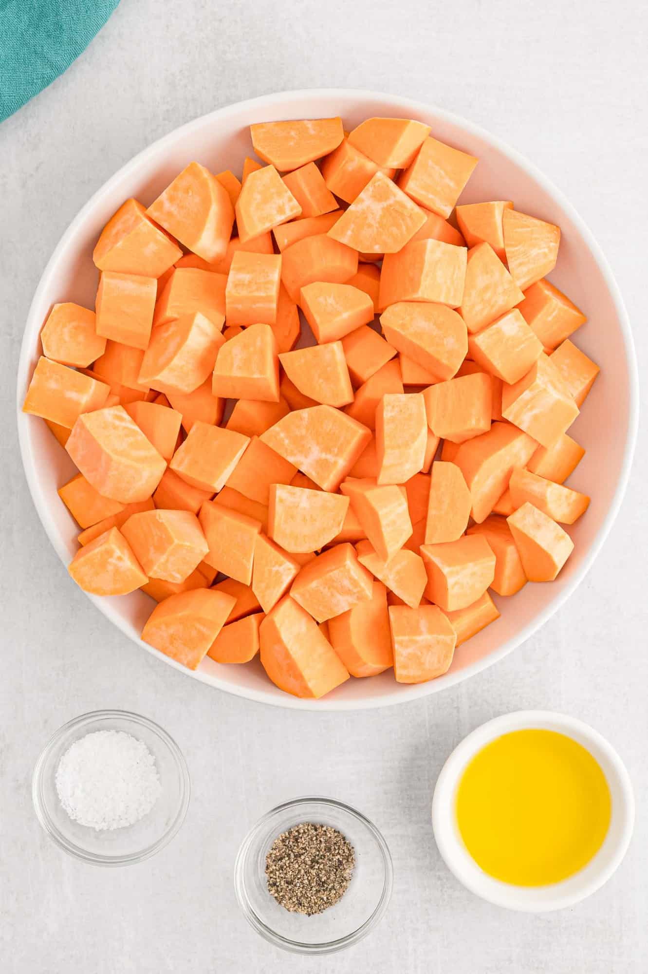 Overhead view of cubed sweet potatoes, olive oil, salt, and pepper.