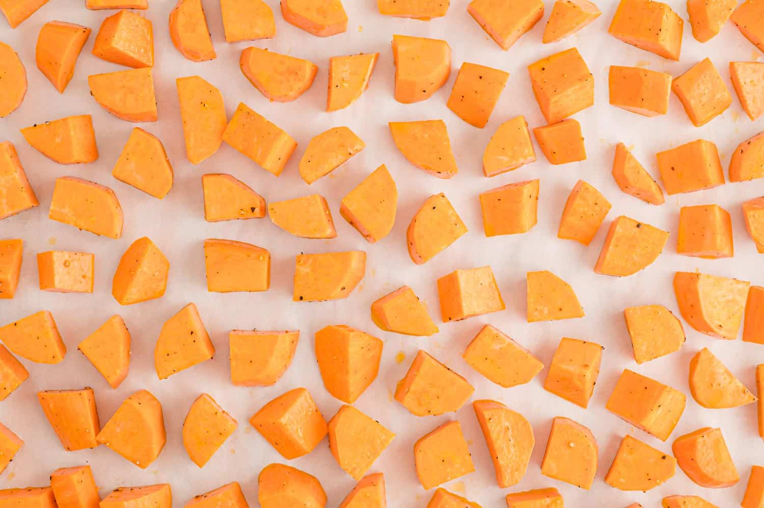 Uncooked sweet potatoes on a parchment paper lined baking sheet.