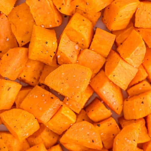 Close up view of cubed roasted sweet potatoes seasoned with salt and pepper.