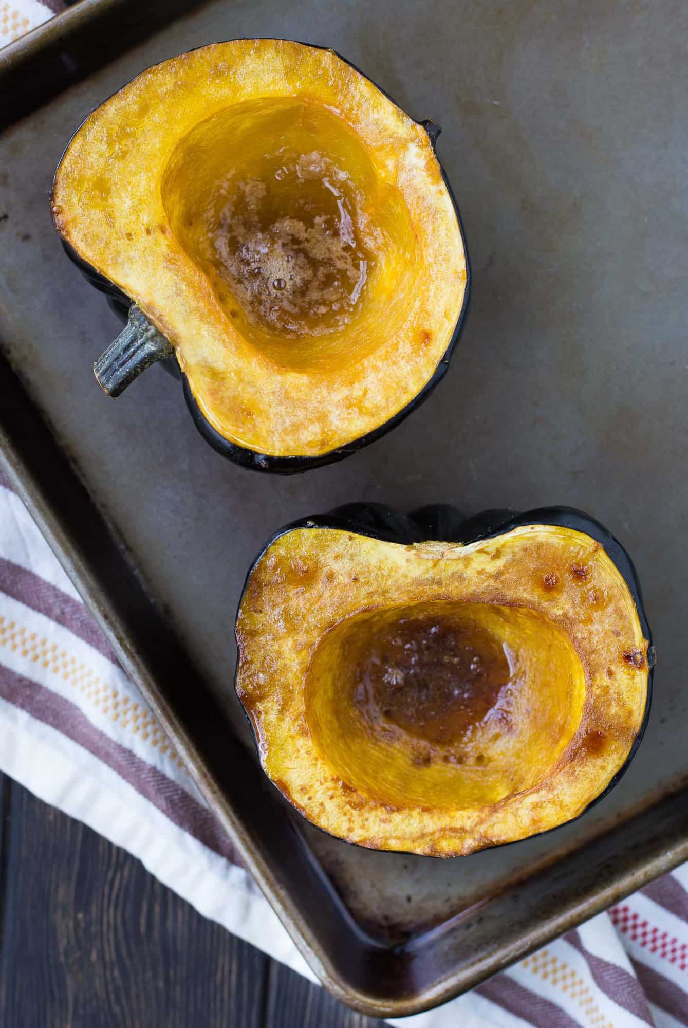 Two halves of roasted acorn squash with brown sugar and butter, on a baking sheet.