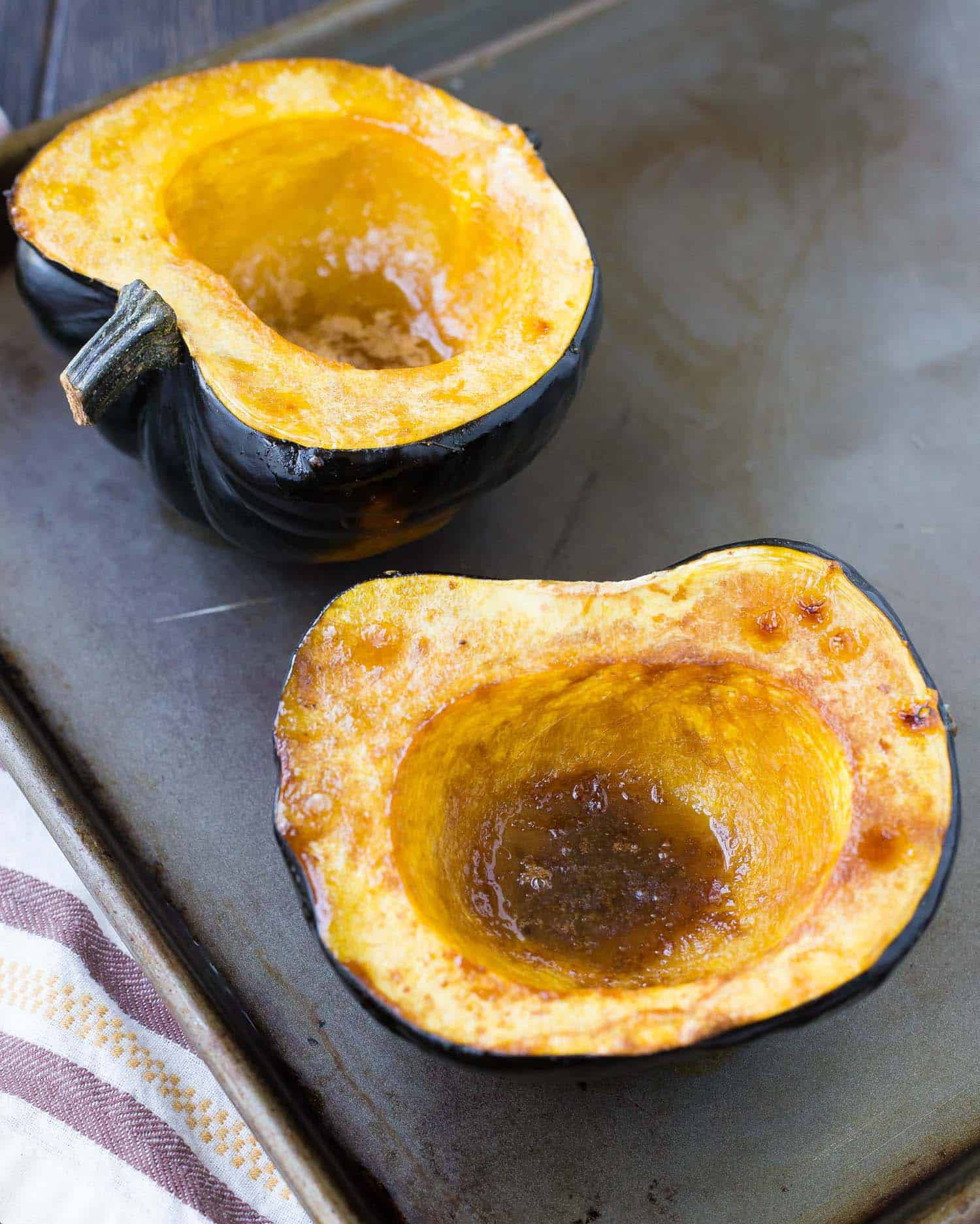 Roasted squash halves on grey baking sheet, filled with melted brown sugar and butter.