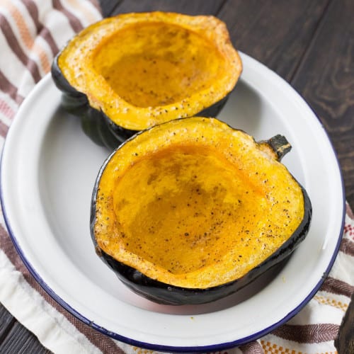 Two acorn squash halves on a white platter, both have been roasted and seasoned with salt and pepper.