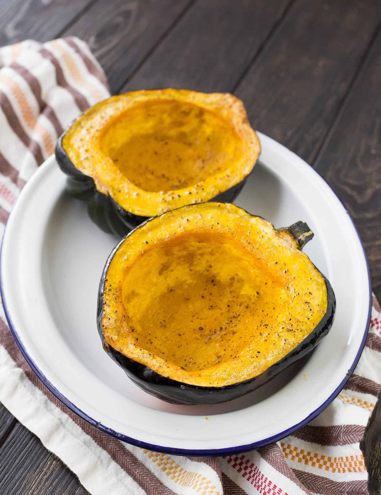 Two acorn squash halves on a white plate. Both have been roasted and seasoned with salt and pepper.