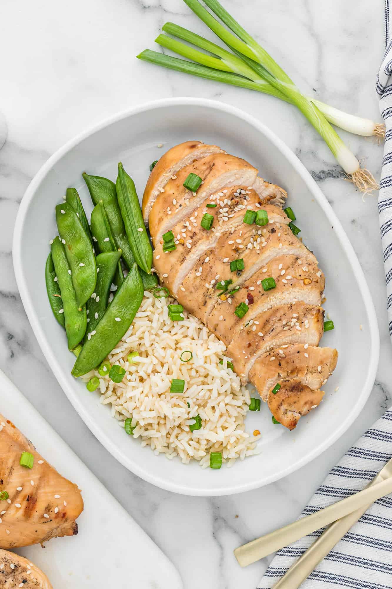 Asian style chicken on a plate with peas and rice.