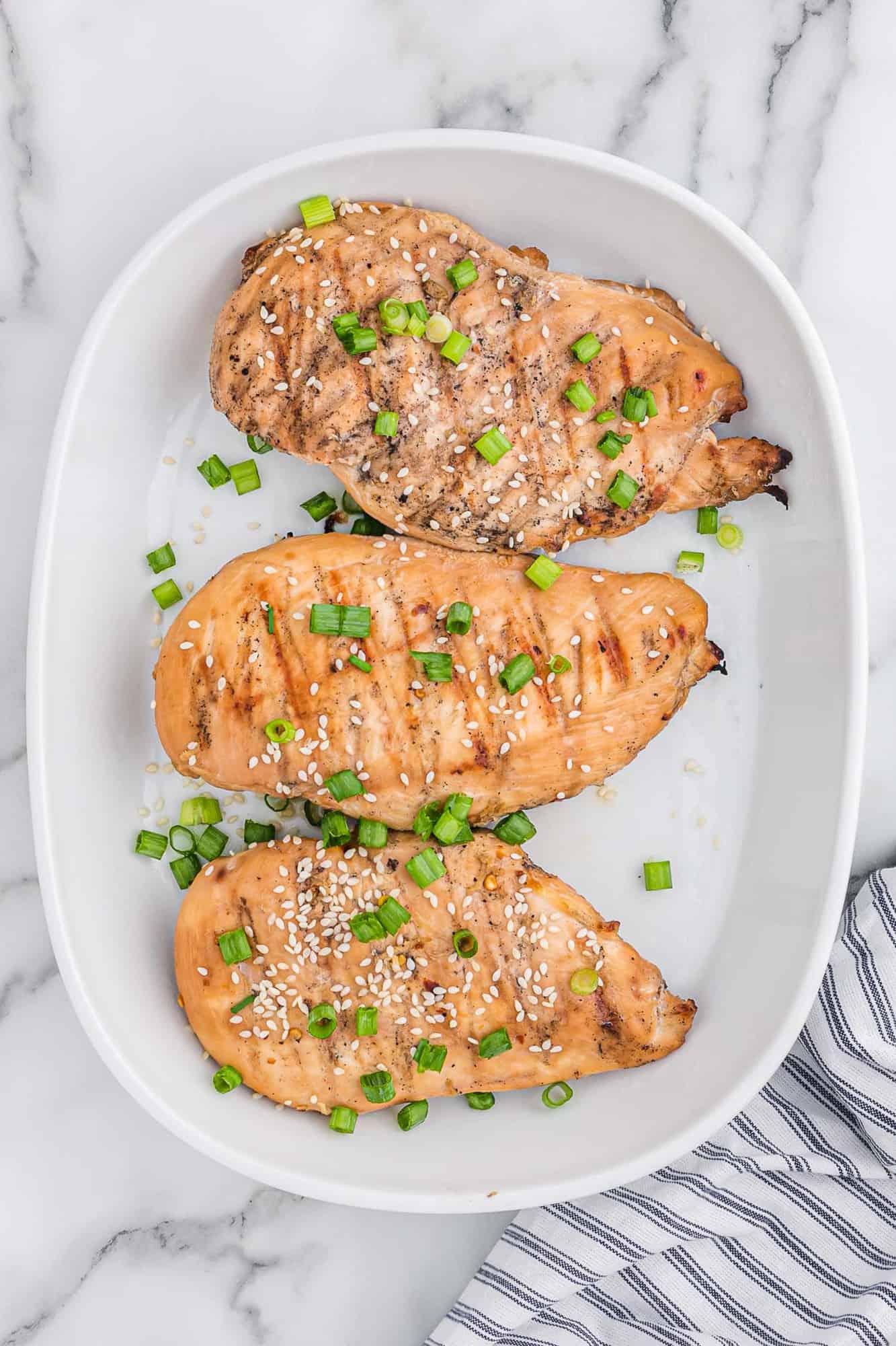 Three cooked chicken breasts on a plate.