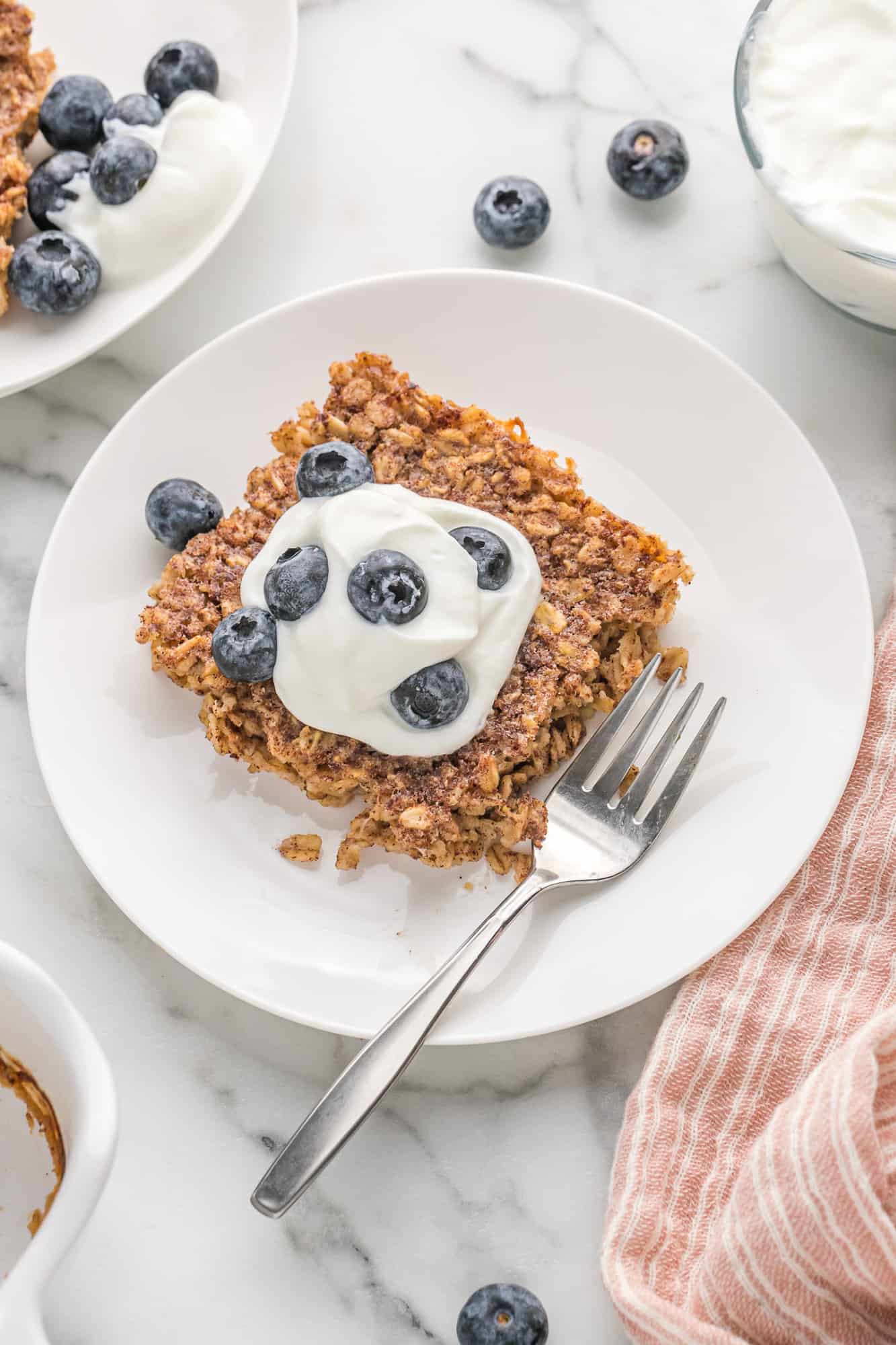 Square of baked oatmeal topped with yogurt and blueberries.