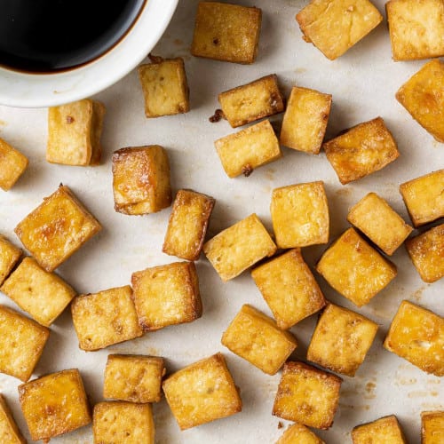 Baked tofu on a baking sheet, soy sauce in the corner of image.