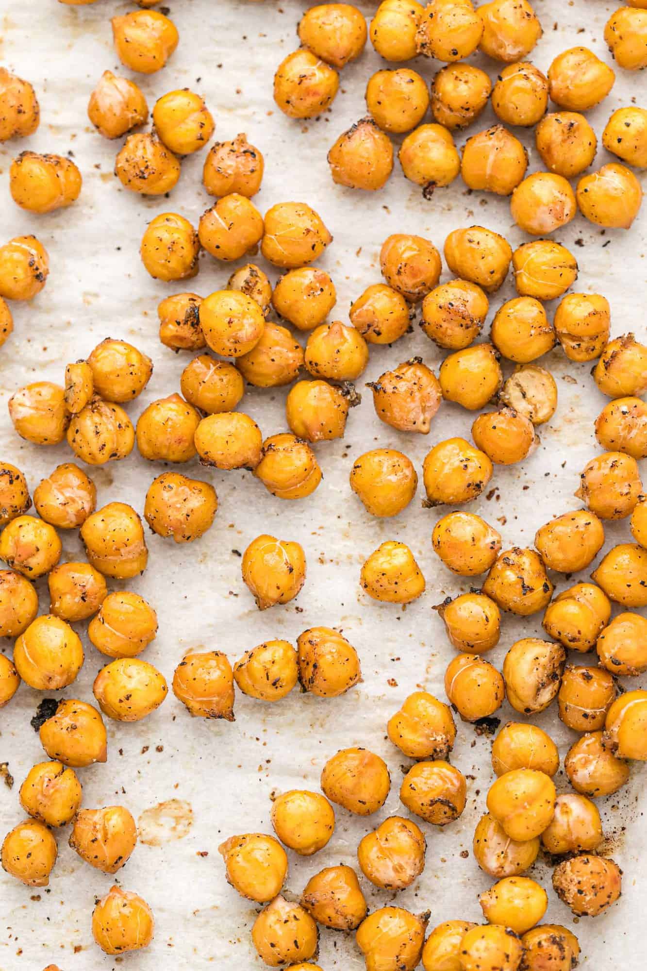 Close up of roasted chickpeas with salt and pepper n a white surface.