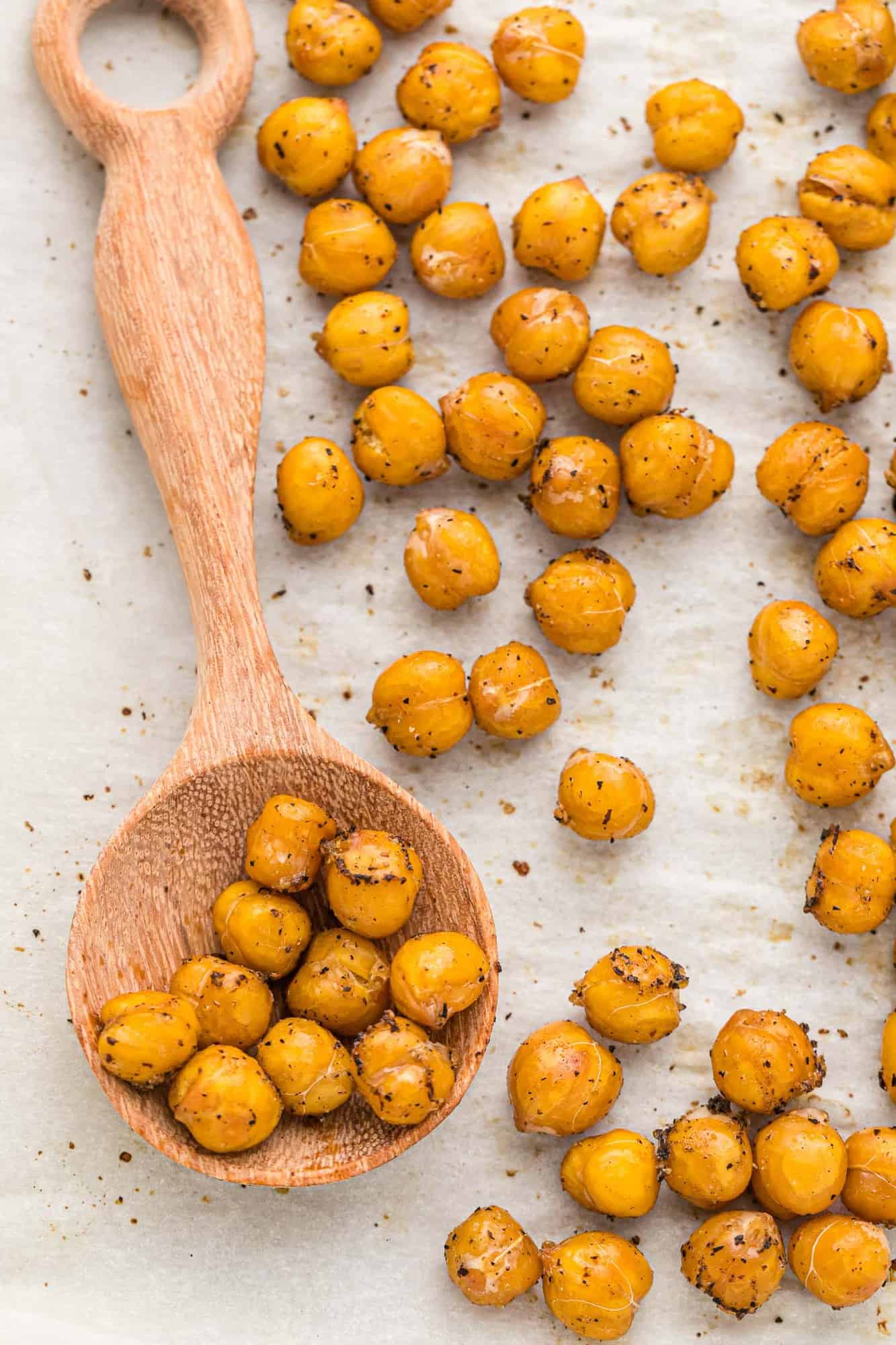 Roasted chickpeas on a parchment lined baking sheet, some on wooden spoon.