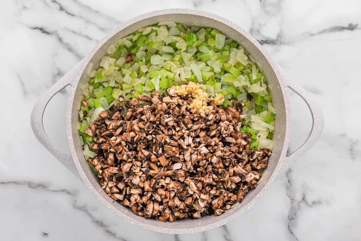 Sauteed onions, celery, and mushrooms in an off white pan.
