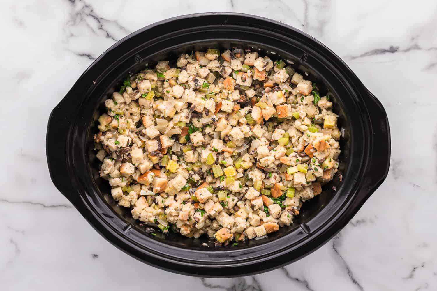 Uncooked stuffing in a black crockpot.