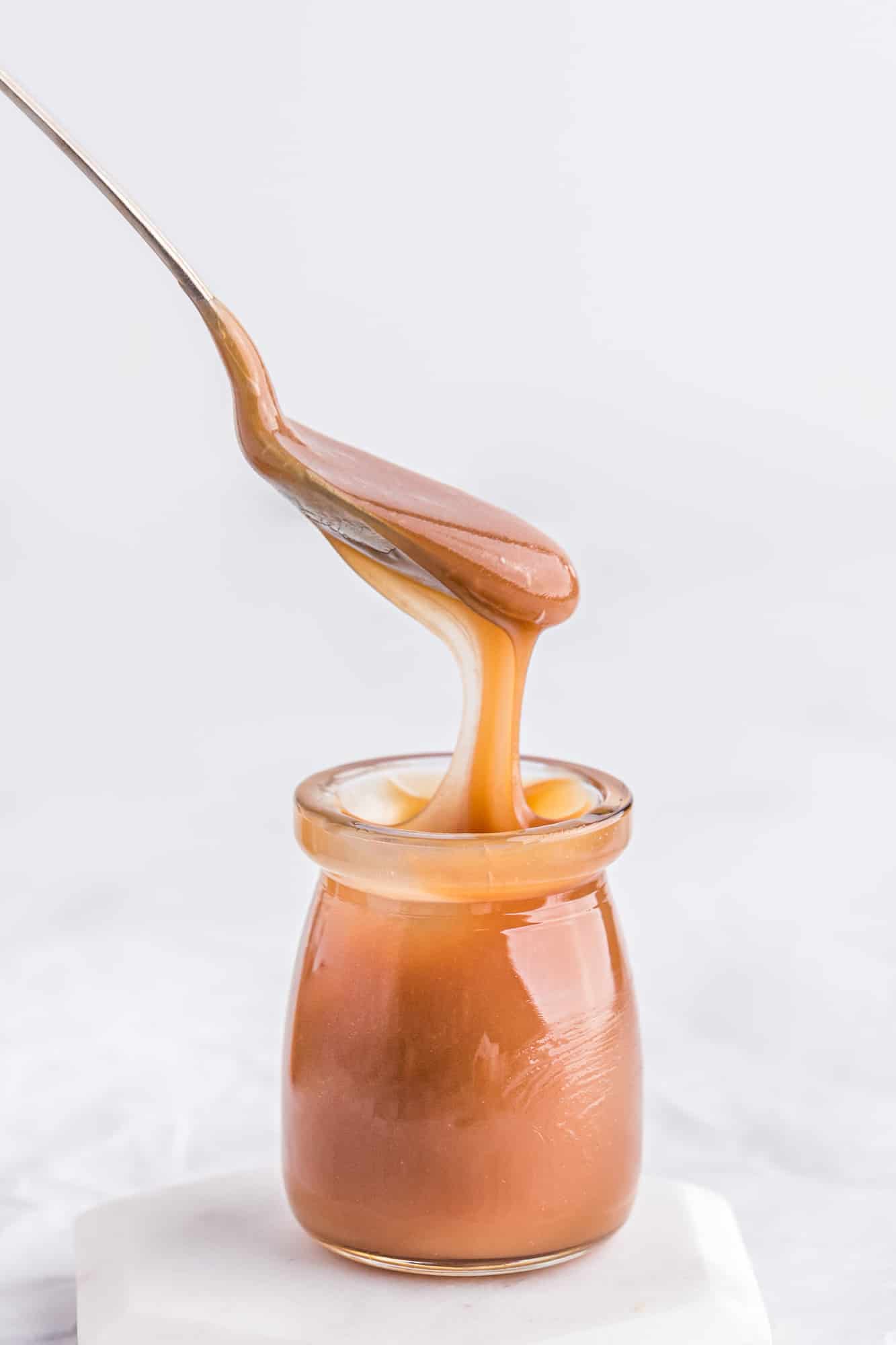 Caramel sauce in a jar, a spoon over it drizzling it into the jar.