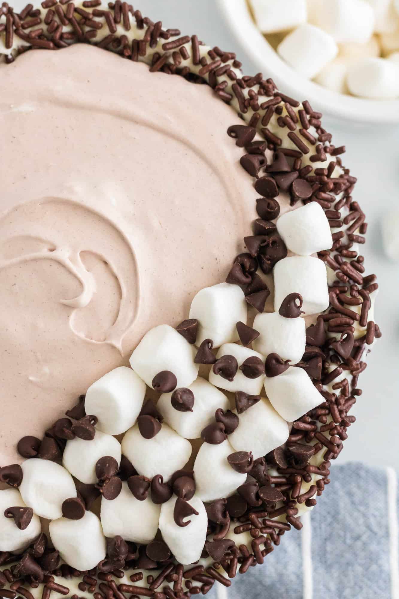 Overhead view of a sprinkle lined bowl filled with hot chocolate dip, topped with marshmallows and chocolate chips.