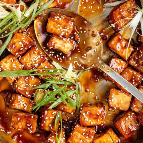 Tofu with a glaze and sesame, some in a spoon.