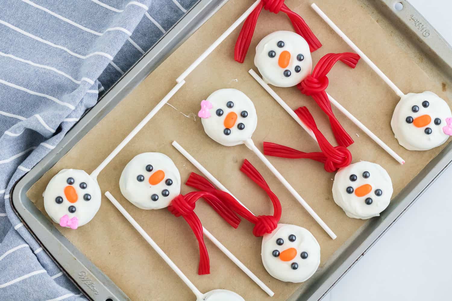 Oreo snowmen pops with scarves on a parchment lined baking sheet.