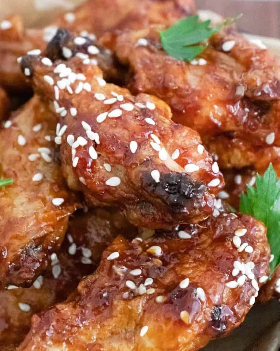 Piile of glazed wings in a basket, sprinkled with sesame seeds.