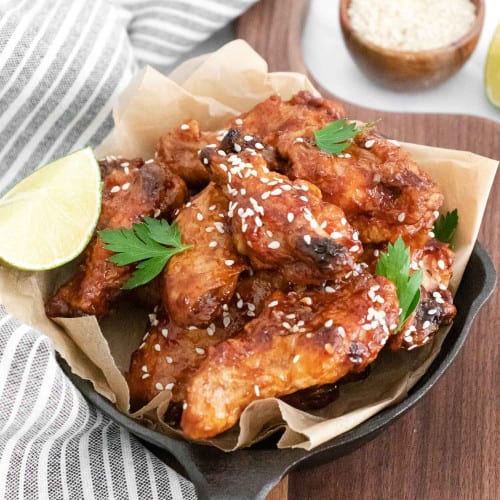 Pan of asian chicken wings sprinkled with sesame seeds and parsley.