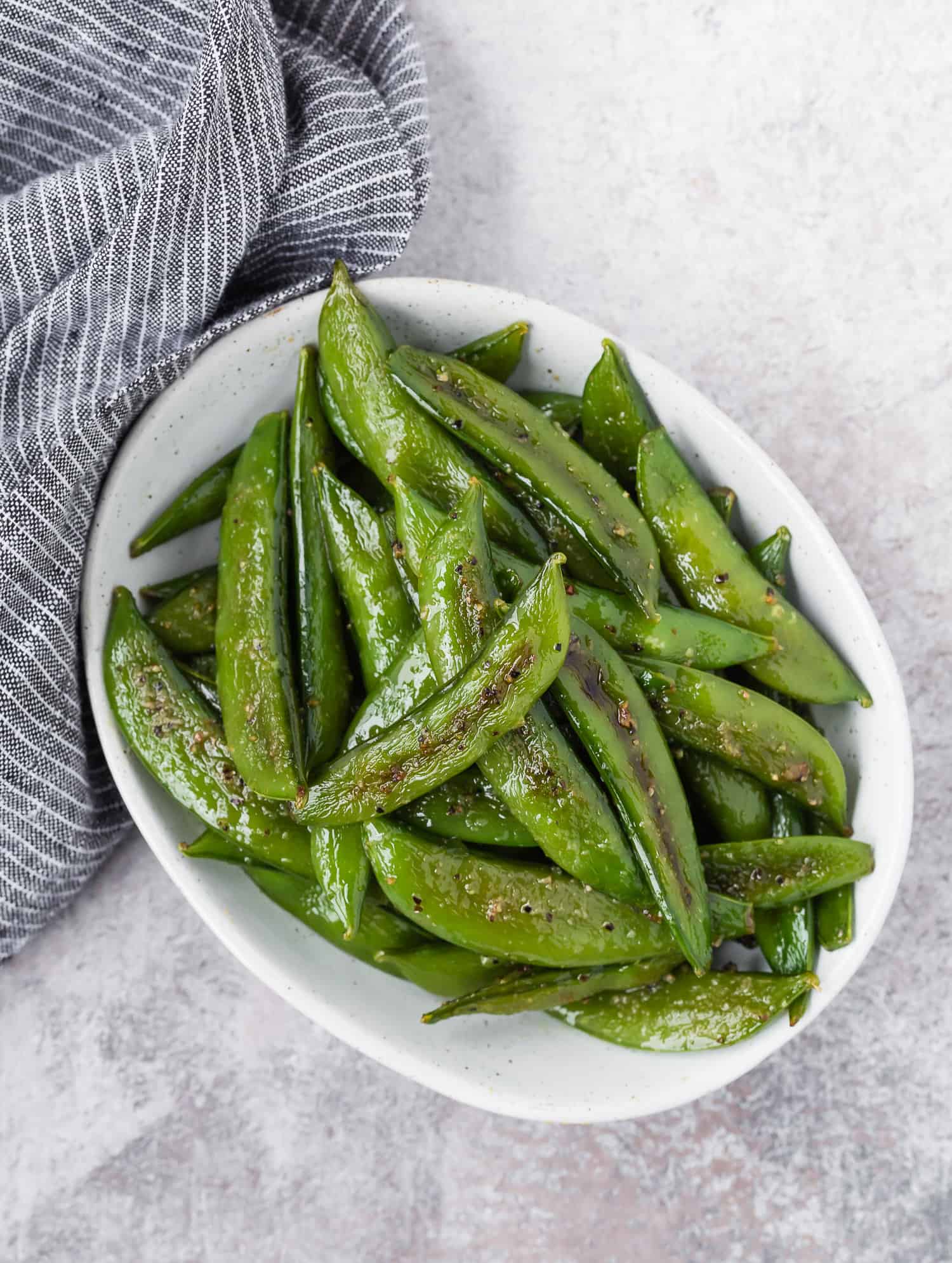 White oval bowl with cooked snap peas in it.