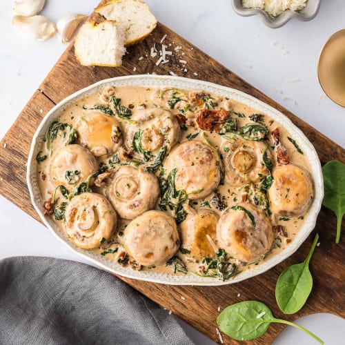 Creamy mushrooms in a oval white bowl, with basil and parmesan.