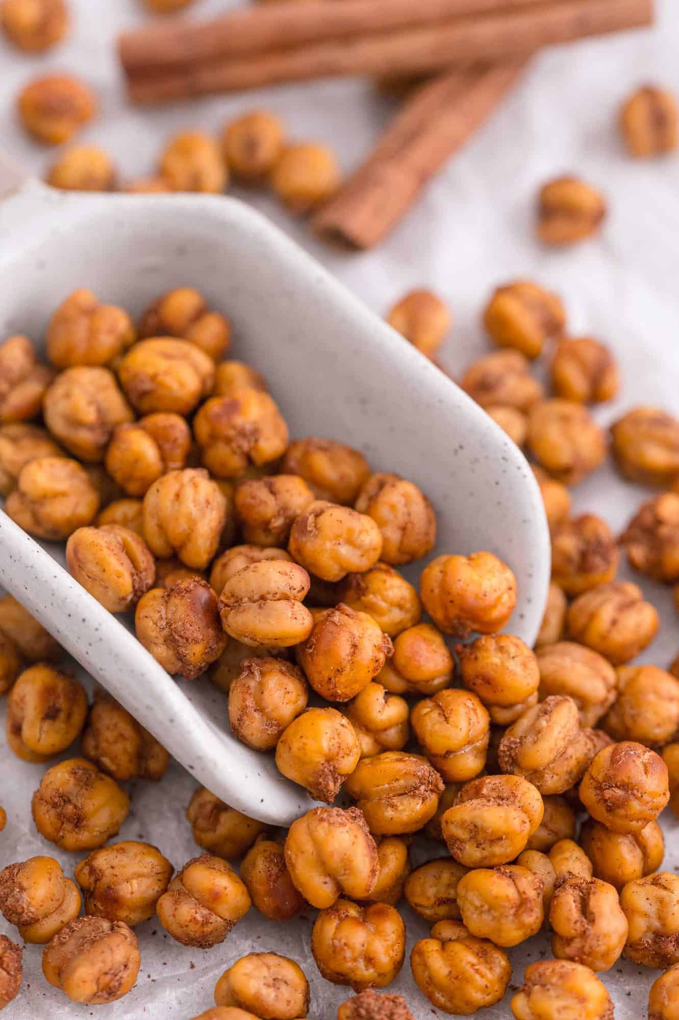 Cinnamon roasted chickpeas pouring out of white scoop.