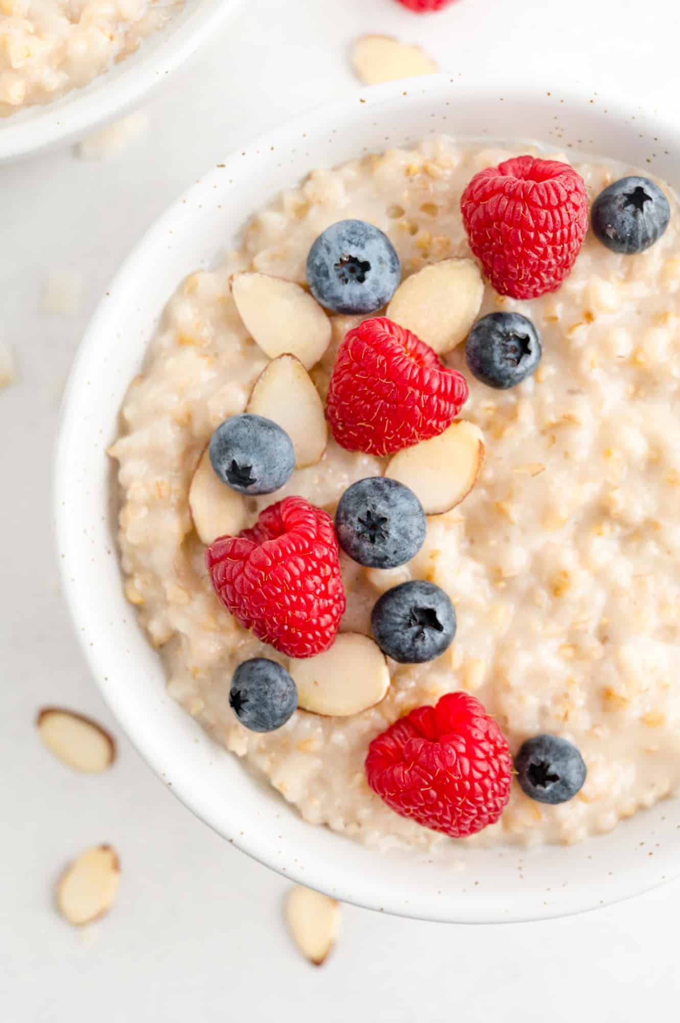 Oatmeal in a white bowl topped with raspberries, blueberries, almonds.