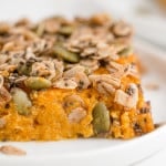 Slice of healthy sweet potato casserole topped with chia seeds, oats, and pepitas.