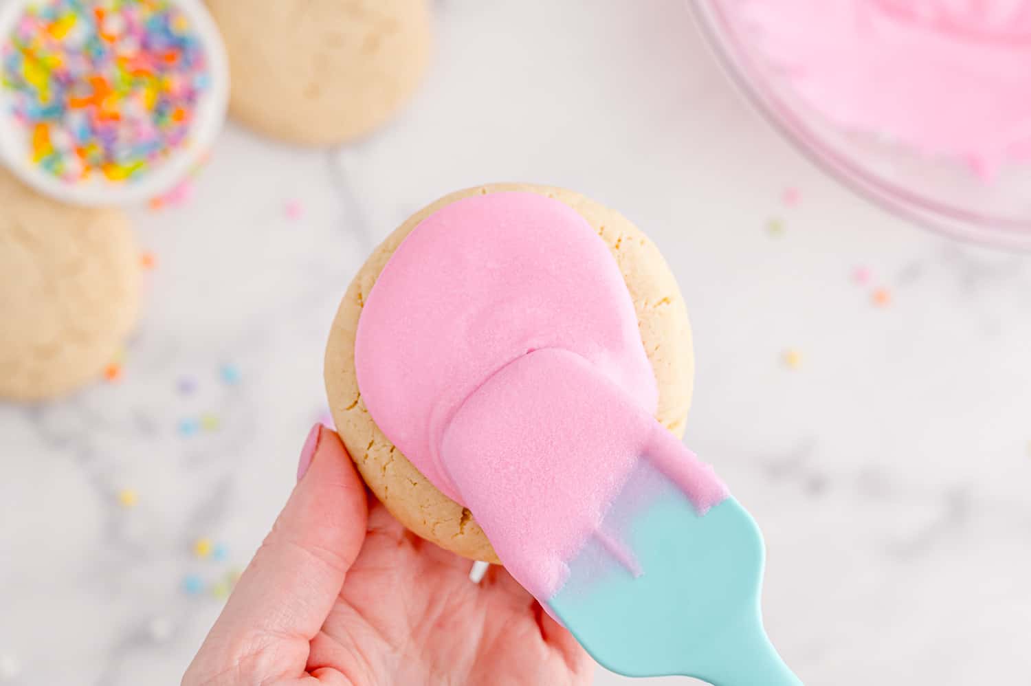Cookie being frosted with pink icing.