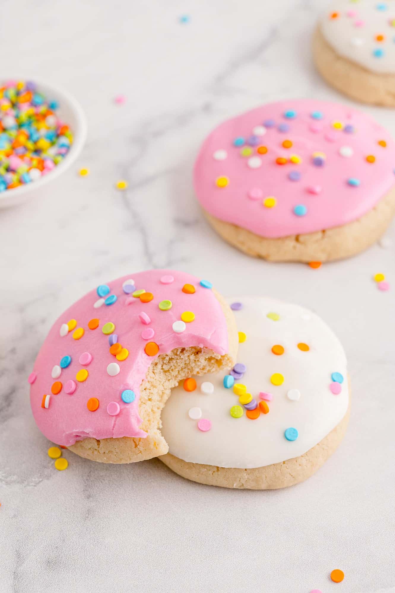 Pink cookie with bite out of it, on top of white frosted cookie.