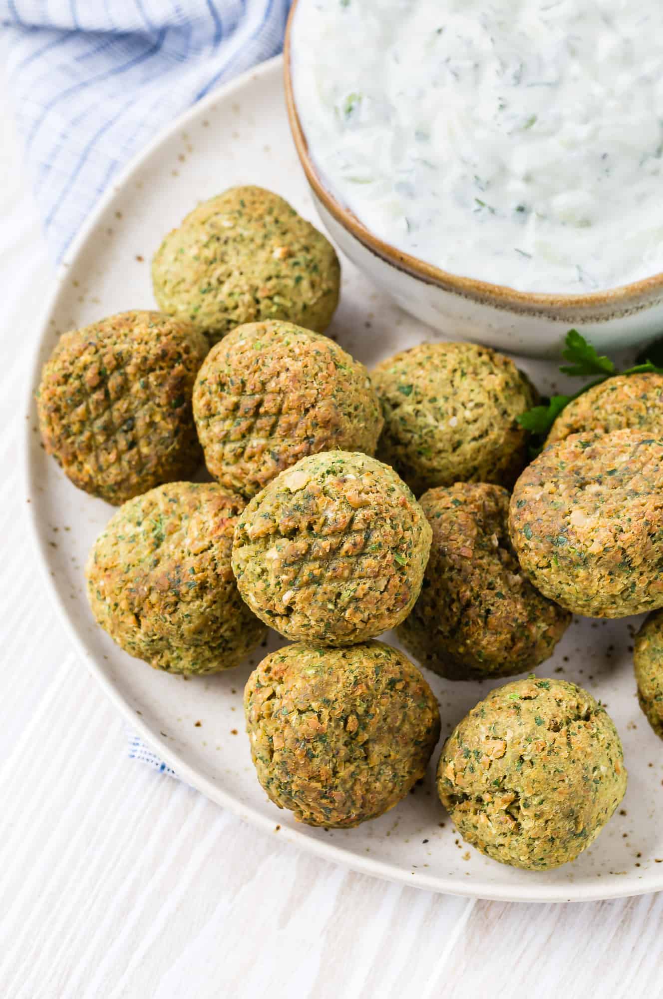 Round golden-brown balls of ground chickpeas and herbs, crispy from an air fryer. A bowl of tzatziki is also pictured. 