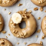 Overhead view of a glazed donut topped with walnuts and a banana slice.