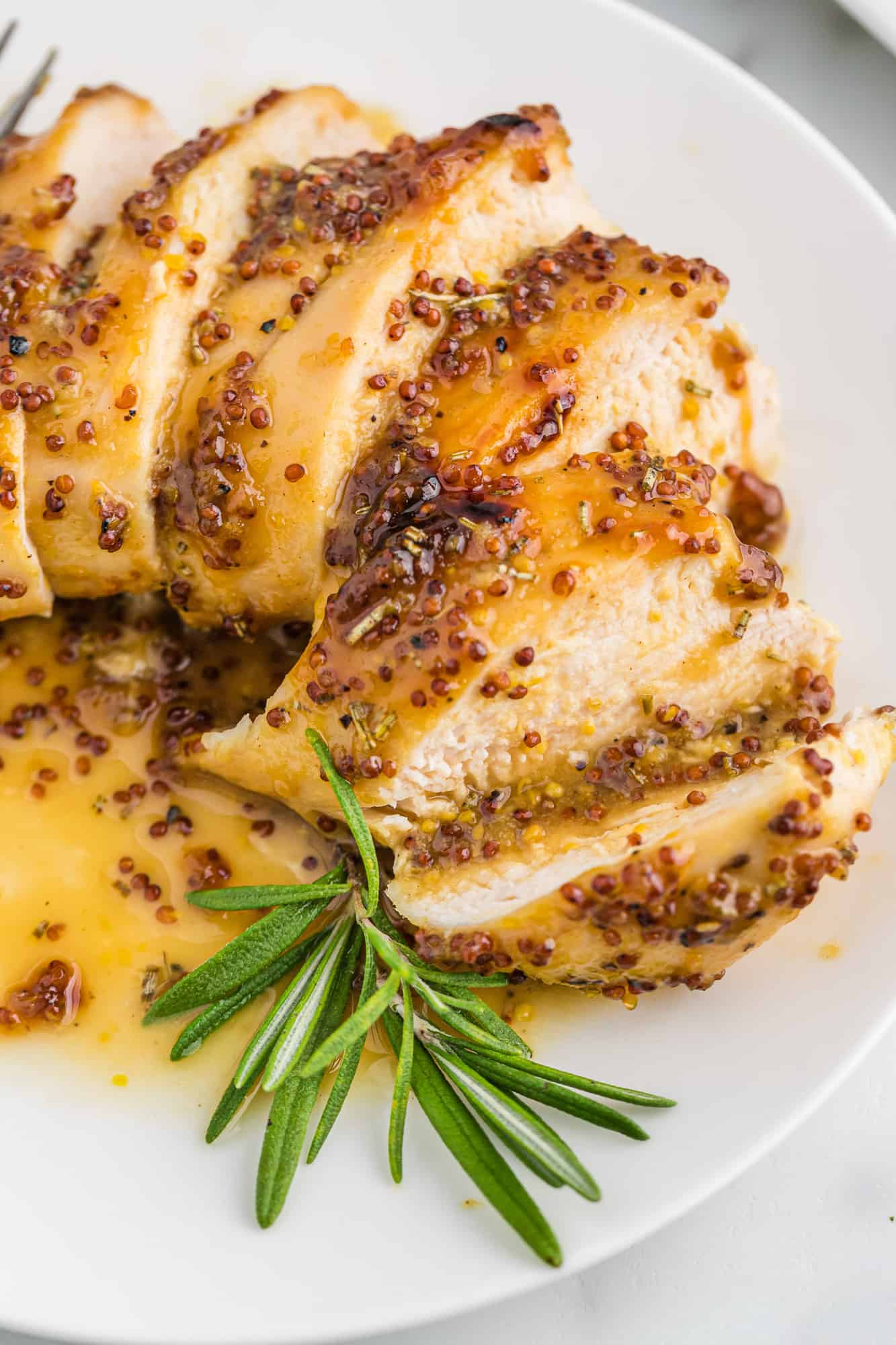 Sliced chicken breast on a plate with honey mustard sauce and fresh rosemary.