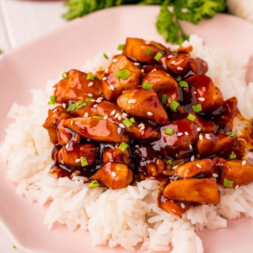 Bourbon chicken served on rice with sesame seeds and green onions.