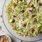 Brussels sprouts salad in a round clear glass bowl, on white marble background.