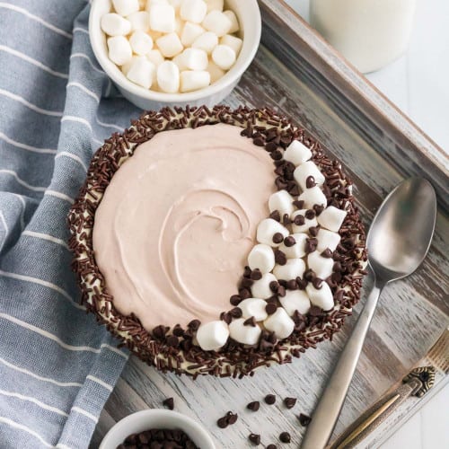 Overhead view of a sprinkle lined bowl filled with hot chocolate dip, topped with marshmallows and chocolate chips.