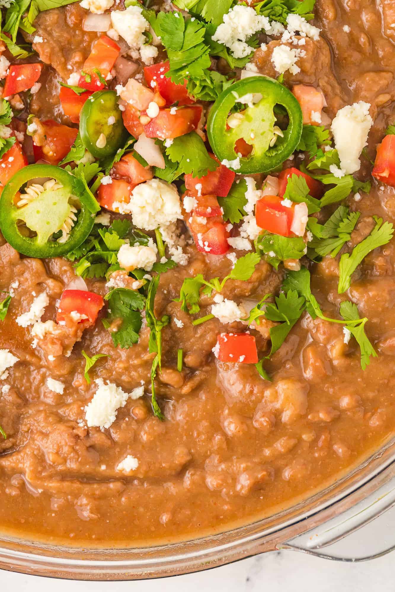 Overhead view of instant pot refried beans topped with cilantro, jalapeno, tomato.