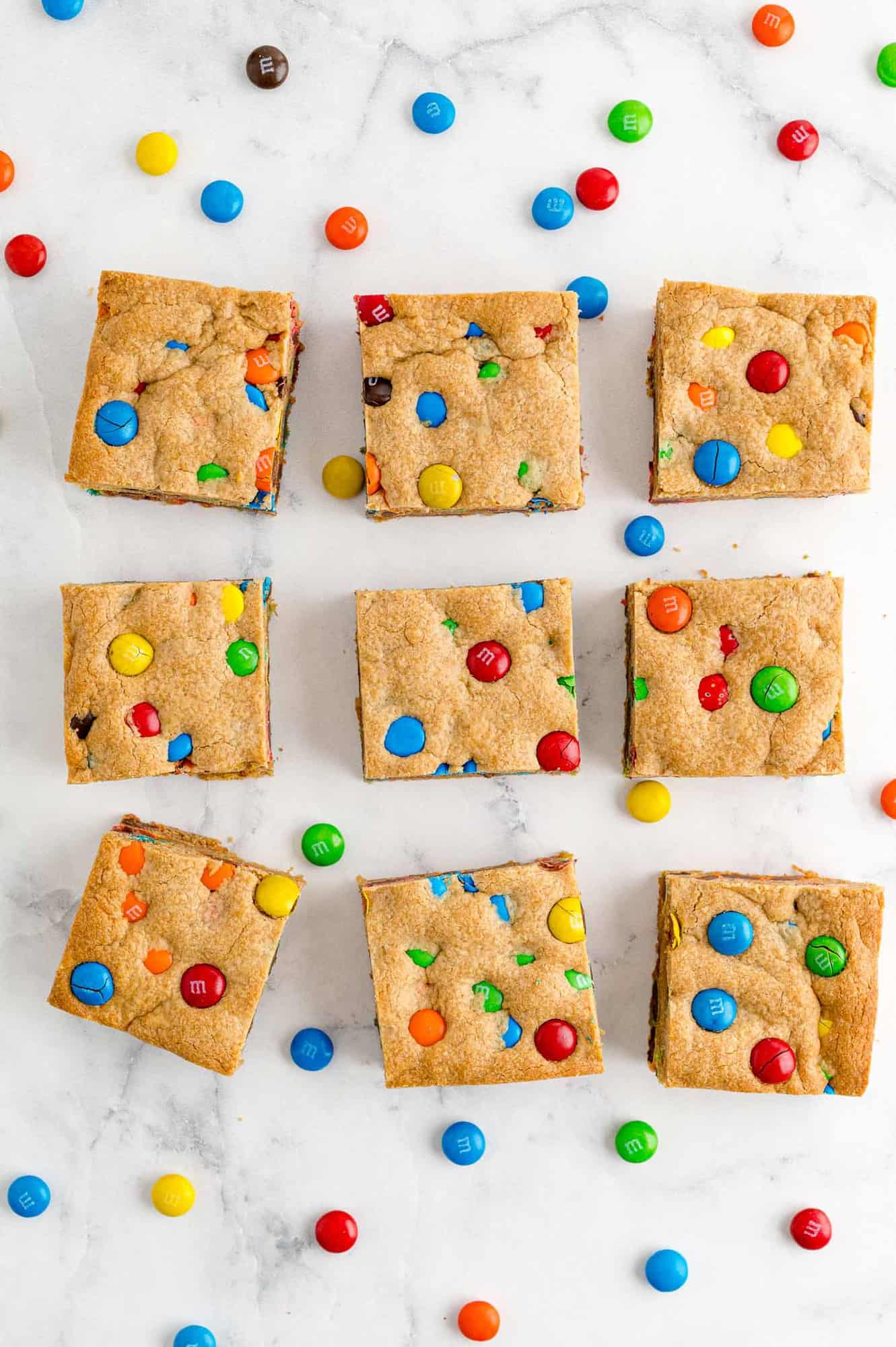 Nine peanut butter bars with M&Ms on white surface.